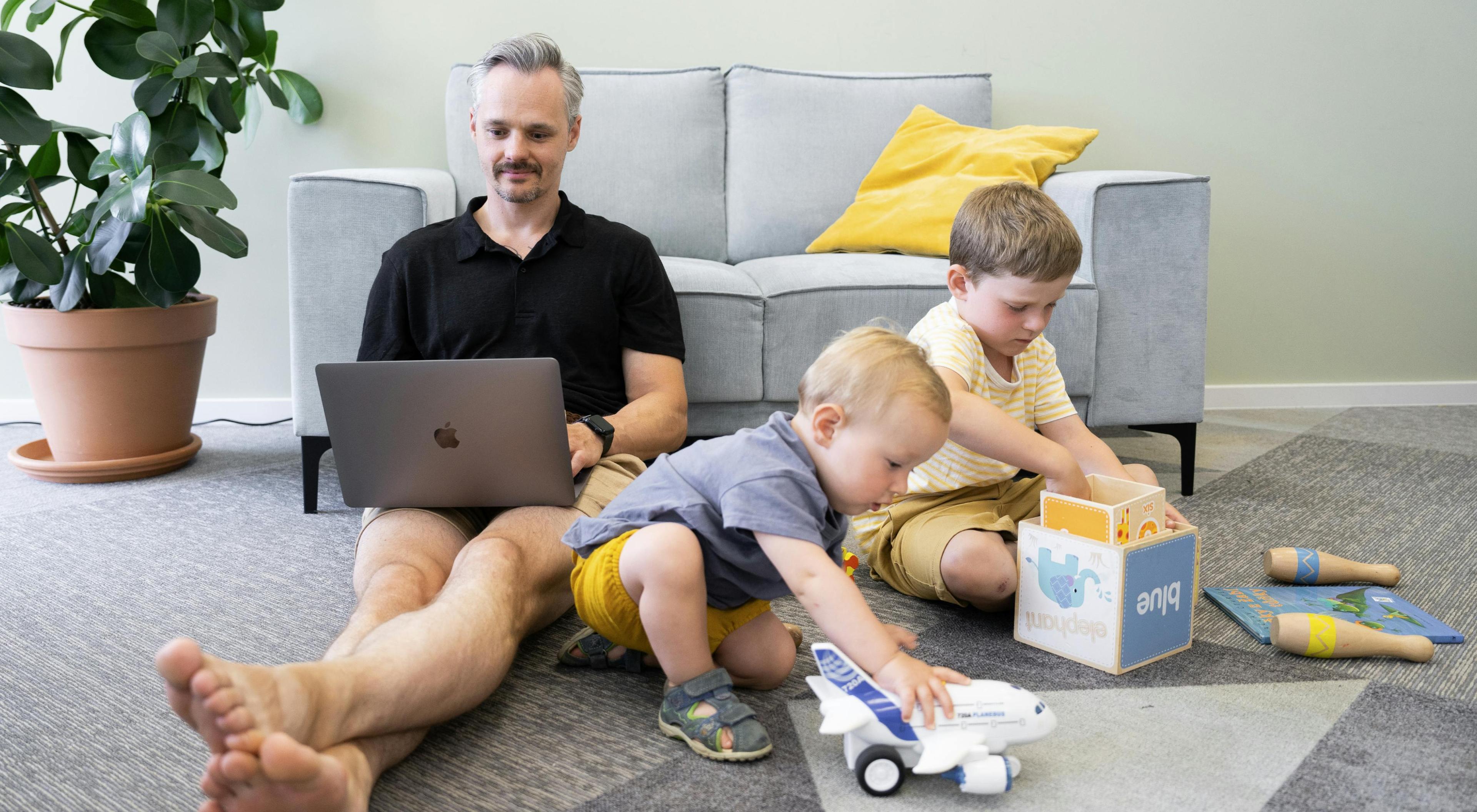 solution architect with a laptop on his lap sitting on the floor next to his children